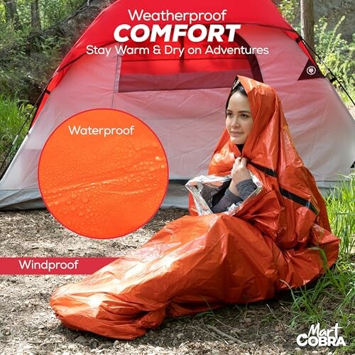 Person in an orange weatherproof sleeping bag sitting outside a tent.